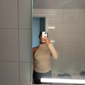 Beige oneshoulder polotopp från Bik Bok - Trendig ribbad polotopp i beige från Bik Bok. Toppen har en unik oneshoulder-design med en lång ärm och hög krage. Perfekt för dig som vill sticka ut med en cool och modern look. Mjuk och stretchig, passar till både jeans och kjol.