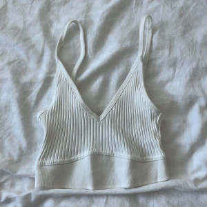 Vit ribbad linnetopp från Zara - Superfräsch vit ribbad linnetopp från Zara med smala axelband och v-ringning. Toppen är croppad och har en bredare kant nedtill som ger en snygg passform. Perfekt till jeans eller kjol för en clean och trendig look.