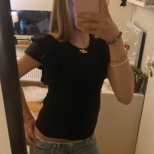 Svart topp med volang från Zara - Säljer en svart topp från Zara i storlek S. Toppen har korta ärmar med snygga volangdetaljer på axlarna och är figurnära i modellen. Perfekt att styla med jeans eller kjol för en trendig och snygg look. Skriv gärna vid frågor! 💞💞💞