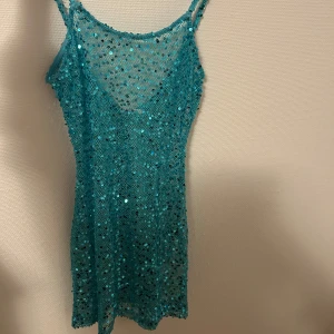 Turkos glittrig kortklänning - Supersnygg turkos kortklänning med tunna axelband och massor av glittrande paljetter. Klänningen har en figurnära passform och är perfekt för dig som vill sticka ut. Perfekt till fest eller när du vill känna dig extra glam. Ny från peppermayo