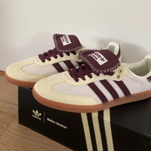 Adidas Wales Bonner Samba sneakers - Unika Adidas Wales Bonner Samba sneakers i beige och vinröd med klassiska tre ränder och kontrastsömmar. Låda, påse och extra sko snöre ingår. Storlek 45. Har använts ett fåtal gånger men det synts inte. Om du har några frågor så fråga bara!