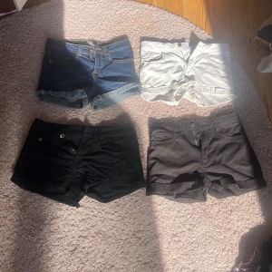 Fyra par shorts i olika färger - Fyra par shorts i olika färger: ett par klassiska blå jeansshorts med upprullade ben, ett par vita shorts, ett par svarta jeansshorts med rå kant och ett par svarta shorts med normal fåll. Perfekta för varma dagar och enkel stil.