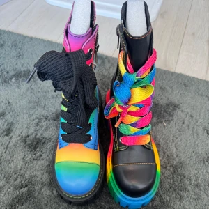 Färgglada boots med regnbågsdetaljer i storlek 38 - Unika boots med chunky plattformssula och regnbågsfärger. Ena skon är helsvart med regnbågsfärgade snören och sula, den andra har regnbågsfärgad ovandel och svarta snören. Båda har dragkedja på sidan och grov sula. Perfekta för dig som vill sticka ut eller för pride. Helt oanvända. Nypris 1200 .