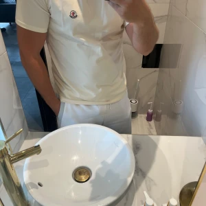 Beige Moncler t-shirt med logga - Snygg beige t-shirt från Moncler med klassisk rund hals och korta ärmar. Stor Moncler-logga framtill i svart och rött samt broderad patch på bröstet. Tillverkad i mjuk bomull för en clean och stilren look.