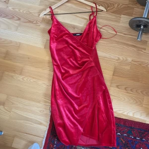 Röd omlottklänning i sammet - Snygg röd omlottklänning i sammet från BIK BOK. Klänningen har smala axelband och en v-ringad design med en slits framtill. Perfekt för en kväll ute eller en speciell tillställning.