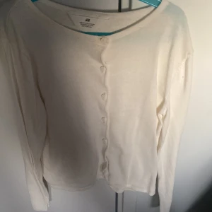 Vit kofta från H&M - Säljer en stilren vit kofta från H&M med knappar framtill. Perfekt för lager-på-lager och passar till många olika outfits. Koftan har långa ärmar och en rund halsringning.