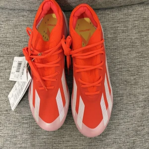 Adidas X Crazyfast Elite F fotbollsskor - Snygga och sportiga Adidas X Crazyfast Elite F fotbollsskor i en iögonfallande röd färg med vita detaljer. Skorna har en strömlinjeformad design med snörning och en lättviktig syntetisk ovandel för optimal hastighet och kontroll på planen. Storlek 39.