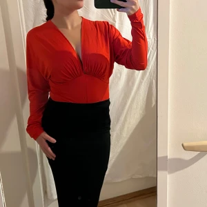 Röd långärmad body - Snygg röd body med långärmade och v-ringad design från H&M. Strlk S. Säljer då den aldrig kommit till användning. 