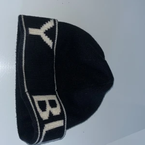 Svart mössa med vit text - Snygg svart mössa med vit text runt om. Perfekt för att hålla värmen under kyliga dagar. Enkel och stilren design som passar till det mesta.