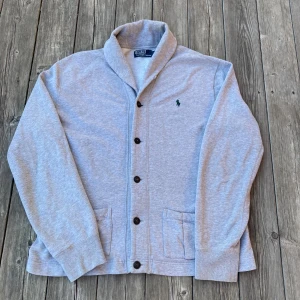 Grå Cardigan från Polo Ralph Lauren - Grå cardigan från Polo Ralph Lauren i mycket bra skick. Storlek L. Inga defekter. Hör av er om frågor!