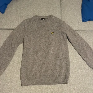 Grå stickad tröja från Lyle & Scott - Säljer en grå stickad tröja från Lyle & Scott med deras ikoniska logga på bröstet. Tröjan har en rund halsringning och långa ärmar. Pris kan sänkas. Stickad i ull. Pass form är M