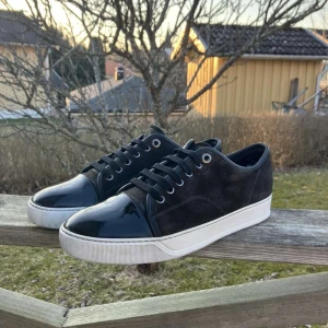 Lanvins - Snygga bruna  sneakers med en kombination av mocka och lackdetaljer på tån. Skorna har en vit sula och snörning framtill. Perfekta för en stilren look.