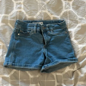 Blå jeansshorts från Cubus - Säljer ett par snygga blå jeansshorts från Cubus. De har en klassisk femficksdesign och är perfekt för sommardagar. Shortsen har en bekväm passform och är lätt att matcha med olika toppar. Perfekt för en avslappnad stil!