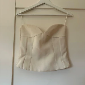 Beige korsettopp från Zara - Säljer en stilren beige korsettopp från Zara med smala axelband och en elegant passform. Perfekt för att skapa en chic look. Toppen har en dragkedja på sidan för enkel på- och avtagning.