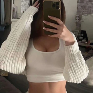 Vit stickad bolerotopp - En vit stickad bolerotopp med långa ärmar. Perfekt för att lägga till en extra touch till din outfit. Den är mjuk och bekväm att bära.