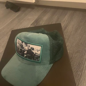 Grön keps med tryck - Snygg grön keps från emilio pendenza med ett unikt tryck på framsidan. Kepsen har ett nätmaterial baktill och en justerbar rem för perfekt passform.