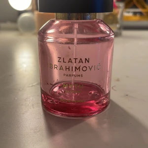 Zlatan Ibrahimović Parfums Myth Bloom - Säljer en elegant parfymflaska från Zlatan Ibrahimović Parfums, modellen Myth Bloom. Flaskan är rosa och rymmer 50 ml. Den har en stilren design med svart kork och guldiga detaljer. Perfekt för den som vill ha en doft med karaktär och stil. Det finns pytte lite kvar går att få ut💕