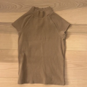 Beige ribbad polotopp - Snygg beige ribbad polotopp med korta ärmar. Perfekt för en stilren look, passar bra till både jeans och kjol. Den har en hög krage som ger en elegant touch.