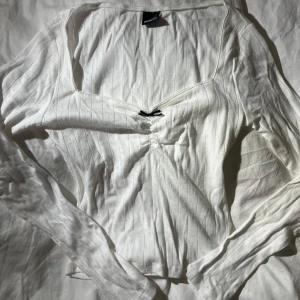 Vit ribbad långärmad topp från Gina Tricot - Säljer en stilren vit ribbad topp från Gina Tricot. Den har långa ärmar och en svart rosett framtill.  Oanvänd 