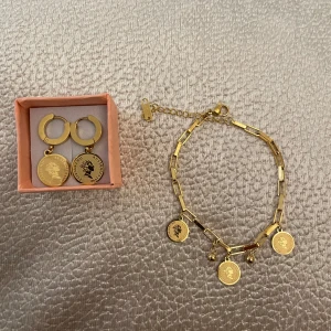Guldörhängen och armband med myntmotiv - Snyggt set med guldörhängen och matchande armband, båda med hängande myntmotiv och är i rostfrittstål.