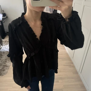 Svart blus  - Svart blus från NA-KD med små volangdetaljer! Super fin nu till våren!