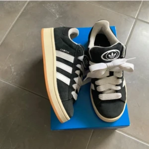 Svarta Adidas Campus 00s sneakers - Nu säljer jag mina trendiga svarta adidas campus 00🤩 sparsamt använda. Storlek 38&2/3💗 Svarta oanvända snören medföljs😊(har allting som medföljdes vid köpet ink lådan)Skorna har en bekväm passform och är perfekta för en stilren look🙌