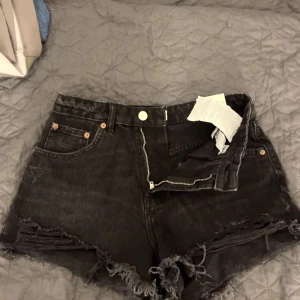 Svarta jeansshorts från Zara - Säljer ett par svarta jeansshorts från Zara med hög midja och fransiga kanter. Shortsen har en dragkedja och knapp framtill. Aldirg kommit till användning❣️