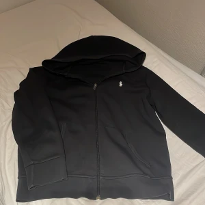 Ralpha lauren zip  - Säljer en stilren svart hoodie från Polo Ralph Lauren med dragkedja och det klassiska logotypbroderiet på bröstet. Perfekt för en avslappnad stil. 