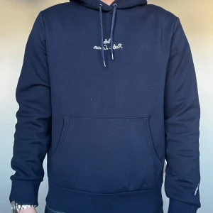 Mörkblå hoodie från Polo Ralph Lauren - Säljer en assnygg mörkblå hoodie från Polo Ralph Lauren med broderad logga på bröstet och en liten broderad detalj på ärmen. Tröjan har en klassisk känguruficka och justerbar huva med snören. Perfekt för en stilren och bekväm look. Aldrig använd!! I helt nyskick!! Köpt i Italien på en polo ralph Lauren butik för 2900kr.