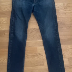 Mörkblå jeansbyxor - Säljer ett par mörkblå jeansbyxor med en klassisk design. Byxorna har en rak passform och är tillverkade i denim. Perfekta för en avslappnad stil.