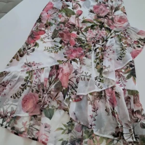 Blommig kjol från Hallhuber - Säljer en vacker blommig kjol från Hallhuber. Kjolen har ett romantiskt mönster med rosa och gröna blommor på en vit bakgrund. Den har volanger som ger en extra touch av elegans. Perfekt för sommarens festligheter! (L ca 80 cm och 70-71 cm I midjan)