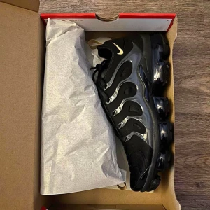 Svarta Nike Vapormax sneakers - Snygga svarta Nike Vapormax sneakers med en futuristisk design och synlig luftdämpning i sulan. Skorna har en diskret Nike-logga och snörning för en säker passform. Perfekta för både stil och komfort.