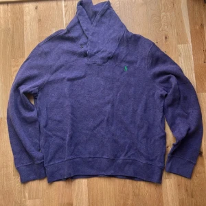 Lila tröja från Polo Ralph Lauren - Säljer en snygg lila tröja från Polo Ralph Lauren i bomull. Tröjan har en broderad grön logga på bröstet och en stilren krage med knappar. Perfekt för en avslappnad stil. För frågor kontakta mig!