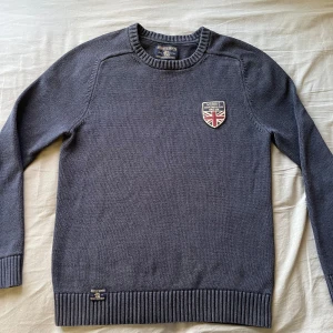 Stickad Morris tröja  - Säljer en stilren mörkblå Morris tröja med ett snyggt märke på bröstet. Tröjan har långa ärmar och ribbade muddar vid ärmslut och nederkant. Perfekt för en casual look! Riktigt snygg nu till hösten och sommaren. Storlek M men passar mer till S. Inga defekter alls utan och är i princip helt ny