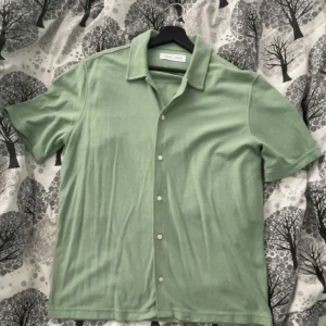 Grön kortärmad skjorta - Snygg grön kortärmad skjorta med knappar framtill. Perfekt för varma dagar och avslappnade tillfällen. Skjortan har en klassisk krage och är tillverkad i ett mjukt material.