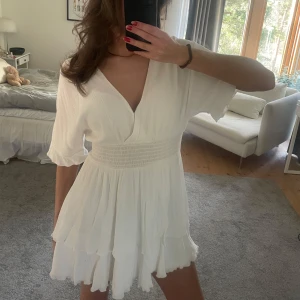 Vit kortklänning med volangdetaljer - Säljer en söt vit kortklänning med v-ringning och volangdetaljer. Klänningen har korta ärmar och en smockad midja som ger en fin passform. Perfekt för sommaren och studenten!!❤️❤️Kolla beskrivningen innan du köper🩷