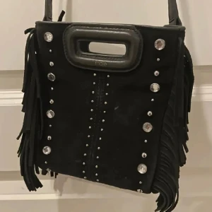 liten svart maje väska  - Snygg svart axelväska med coola fransar och nitar. Väskan är från maje och är använd max 15 gånger. väskan är i den minsta modellen men får plats med en del ändå. Inga stora skador men lite av maje märket är borta. Ny priset var 1200 kr men jag säljer för, 700kr.🤍🫶🏽
