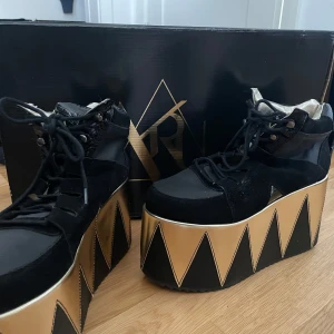 Svarta platåskor från Y.R.U - Unika svarta platåskor från Y.R.U med guld detaljer. Skorna har snörning och en kraftig platå som ger extra höjd. 