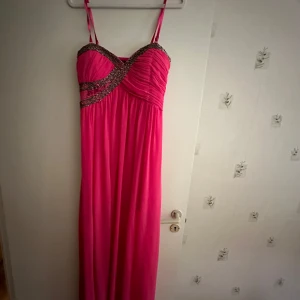 Rosa långklänning från Little Mistress - Säljer en fantastisk rosa långklänning från Little Mistres!Lång klänning med utsmyckning vid byst, med slits och underkjol.  Storlek M/L. Längd till slits 85 cm. Klänning längd 150 cm Man kan ta av bandet och dom är justerbara.Gummi på ryggen så det töjer sig bra och anpassa sig till kroppen.Helt nytt. M/L