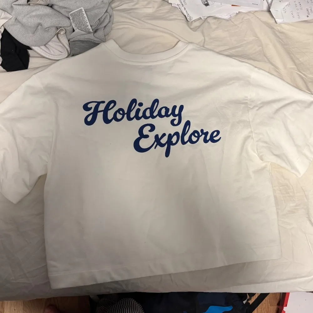 Säljer en vit t-shirt med blått tryck 'Holiday Explore' på både fram- och baksidan. T-shirten har en avslappnad passform och korta ärmar, perfekt för en ledig stil. Den har aldrig använts och har prislappen kvar. Den är lite för stor på mig som är S men borde passa perfekt på M💕. T-paidat.