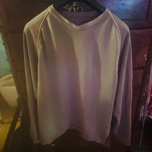 Beige långärmad tröja med broderade initialer KV Kriminalvården  - Säljer en stilren beige långärmad tröja med v-ringning. Tröjan har broderade initialer 'KV' på ärmen, vilket ger en personlig touch. Kriminalvården 