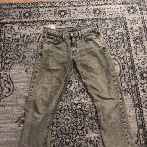 Grå Levis 502 jeans - Säljer ett par grå Levis 502 jeans med en klassisk femficksdesign. De har en normal passform och är tillverkade i denim. Perfekta för en avslappnad stil.