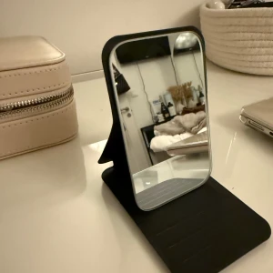 Svart hopfällbar sminkspegel - Praktisk och stilren svart hopfällbar sminkspegel. Perfekt för resor eller att ha i handväskan. Enkel att ställa upp och fälla ihop för smidig förvaring.