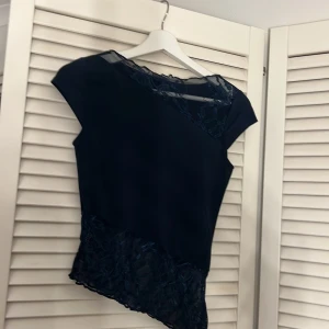 Mörkblå topp med spetsdetaljer - Snygg mörkblå topp med spetsdetaljer vid hals och nederkant. Kortärmad design som ger en elegant touch. Perfekt för en stilren look.