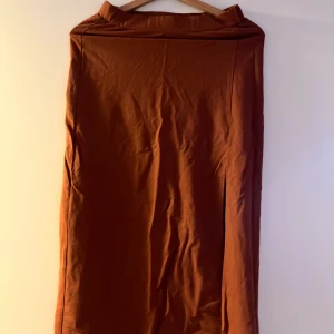 Brun kjol från Gina Tricot - Snygg brun kjol från Gina Tricot i en klassisk design. Kjolen har en slits på sidan som ger en elegant touch. Perfekt för olika tillfällen och lätt att matcha med olika toppar.