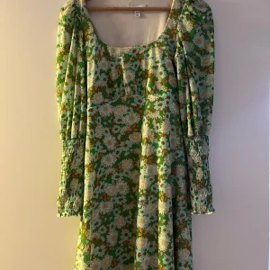 Blommig klänning från Topshop - Säljer en färgglad blommig klänning från Topshop med gröna och vita nyanser. Klänningen har långa ärmar och en fyrkantig urringning. Perfekt för en somrig look!