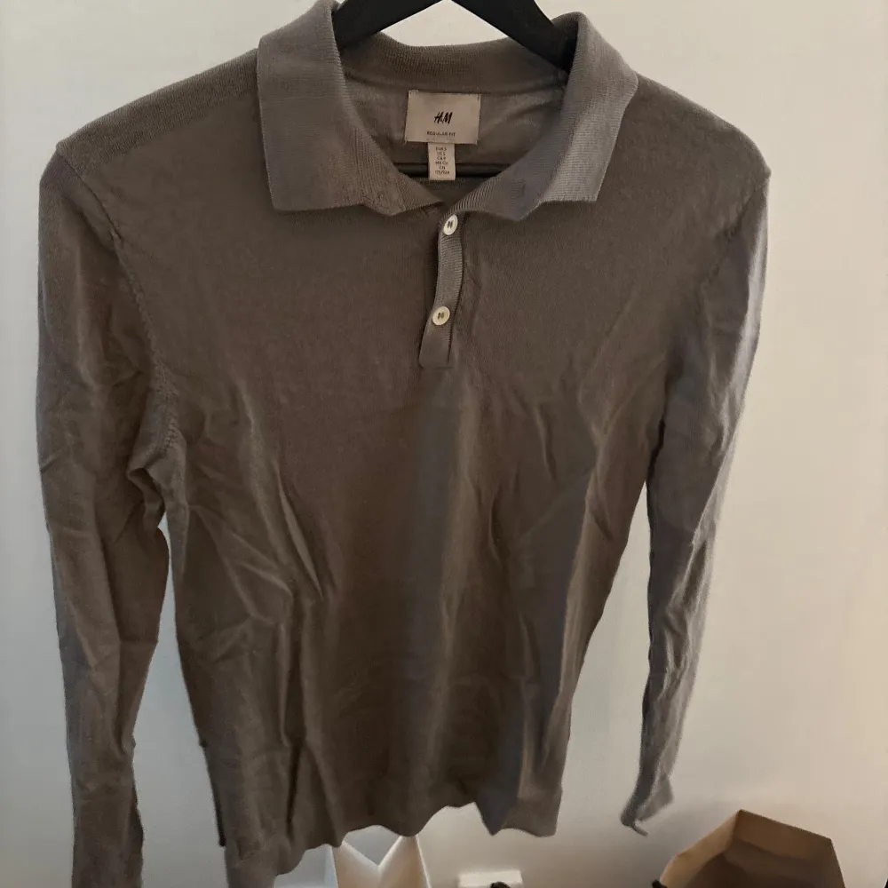 Säljer en stilren grå långärmad pikétröja från H&M. Tröjan har en klassisk krage med två knappar och är tillverkad i 100% ull, vilket gör den både bekväm och varm. Perfekt för kyligare dagar.. Neuletakit & Villapaidat.