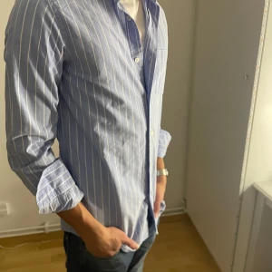 Blåvitrandig linneskjorta från Massimo Dutti - Linneskjorta i blåvitt mönster från Massimo Dutti. Funkar hur bra somhelst nu till vår- och sommarsäsong. Plagget är sparsamt använd och är i väldigt gott skick! Tveka inte att höra av dig vid frågor eller funderingar.