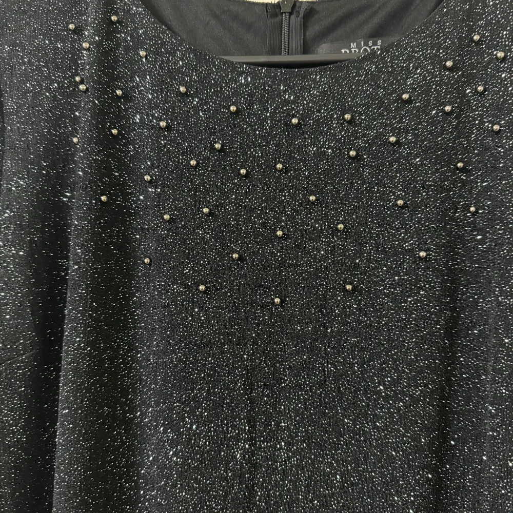 Elegant svart ärmlös klänning med glittriga detaljer längs nederkanten. Perfekt för en kväll ute eller en speciell tillställning. Klänningen har en stilren design med en rund halsringning.. Mekot.