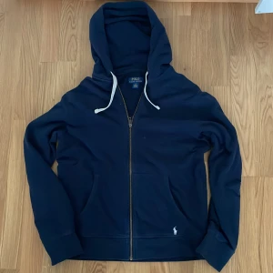 Mörkblå hoodie från Polo Ralph Lauren - Säljer en snygg mörkblå hoodie från Polo Ralph Lauren. Den har en dragkedja framtill och en justerbar huva med vita snören. Perfekt för en avslappnad stil. Skriv gärna vid frågor